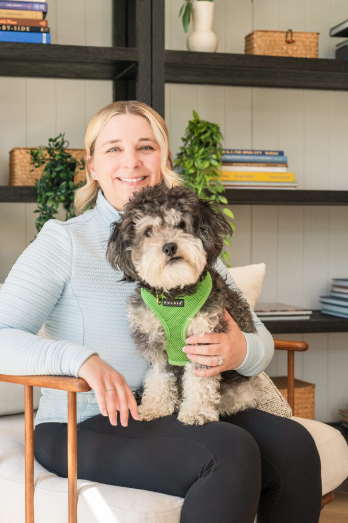 Girl holding a gray and white dog wearing a green harness.